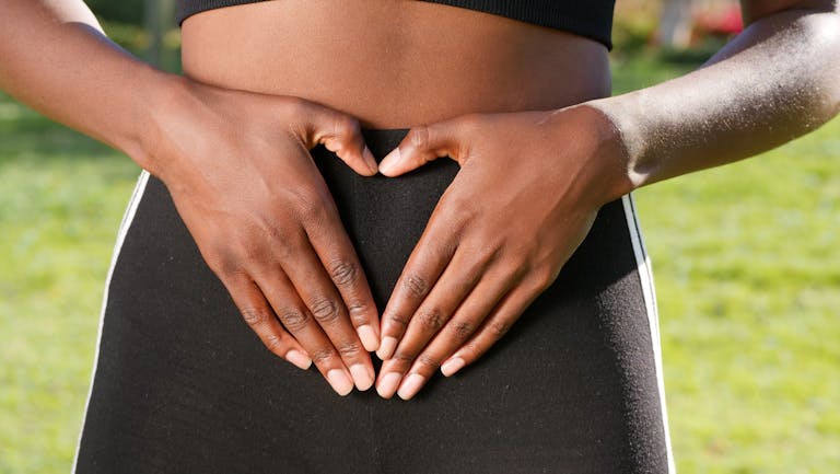 Close-up of hands forming a heart shape on woman's belly, symbolizing health and love.