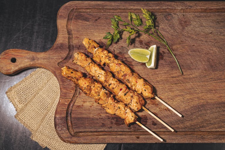 Juicy grilled chicken skewers on a wooden board with lime and herbs.