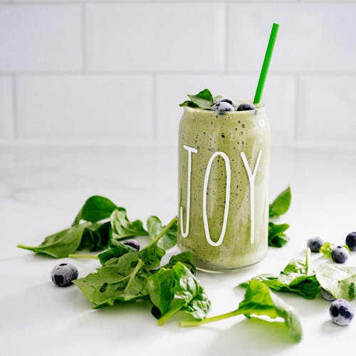 Refreshing green smoothie with spinach and blueberries in a glass labeled 'JOY' on a white background.