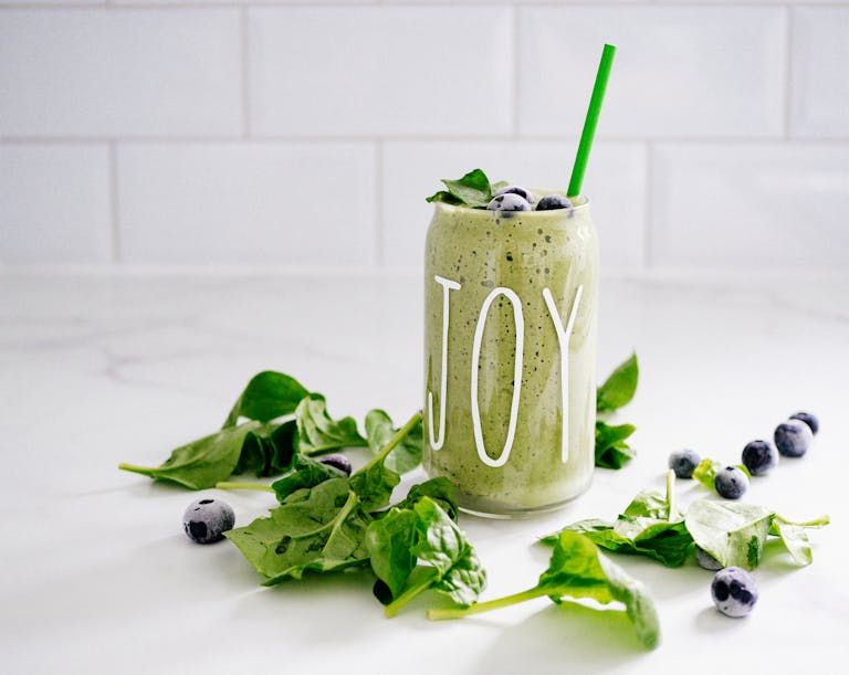 Refreshing green smoothie with spinach and blueberries in a glass labeled 'JOY' on a white background.