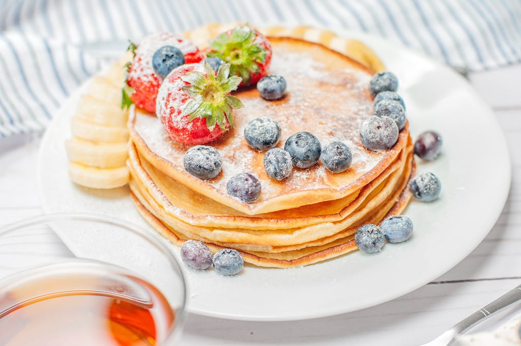 Stack of pancakes topped with fresh strawberries, blueberries, and banana slices, perfect for breakfast.