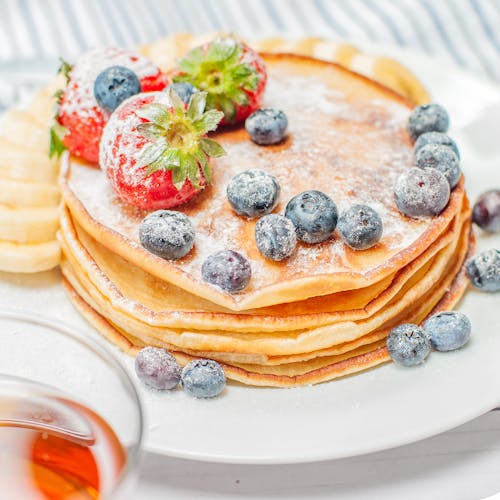 Stack of pancakes topped with fresh strawberries, blueberries, and banana slices, perfect for breakfast.