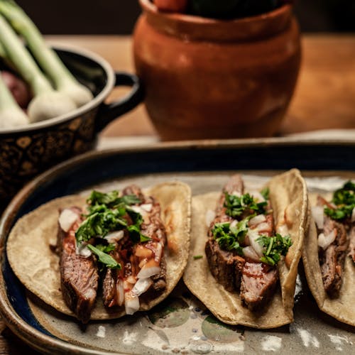 Three mouth-watering steak tacos topped with cilantro and onions on a rustic table setting.