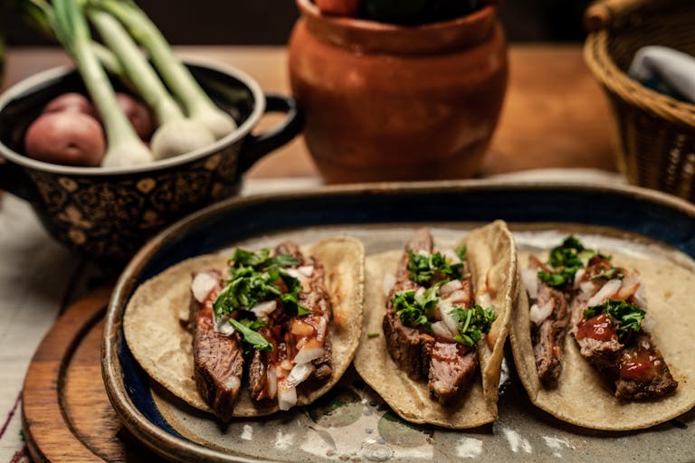 Three mouth-watering steak tacos topped with cilantro and onions on a rustic table setting.