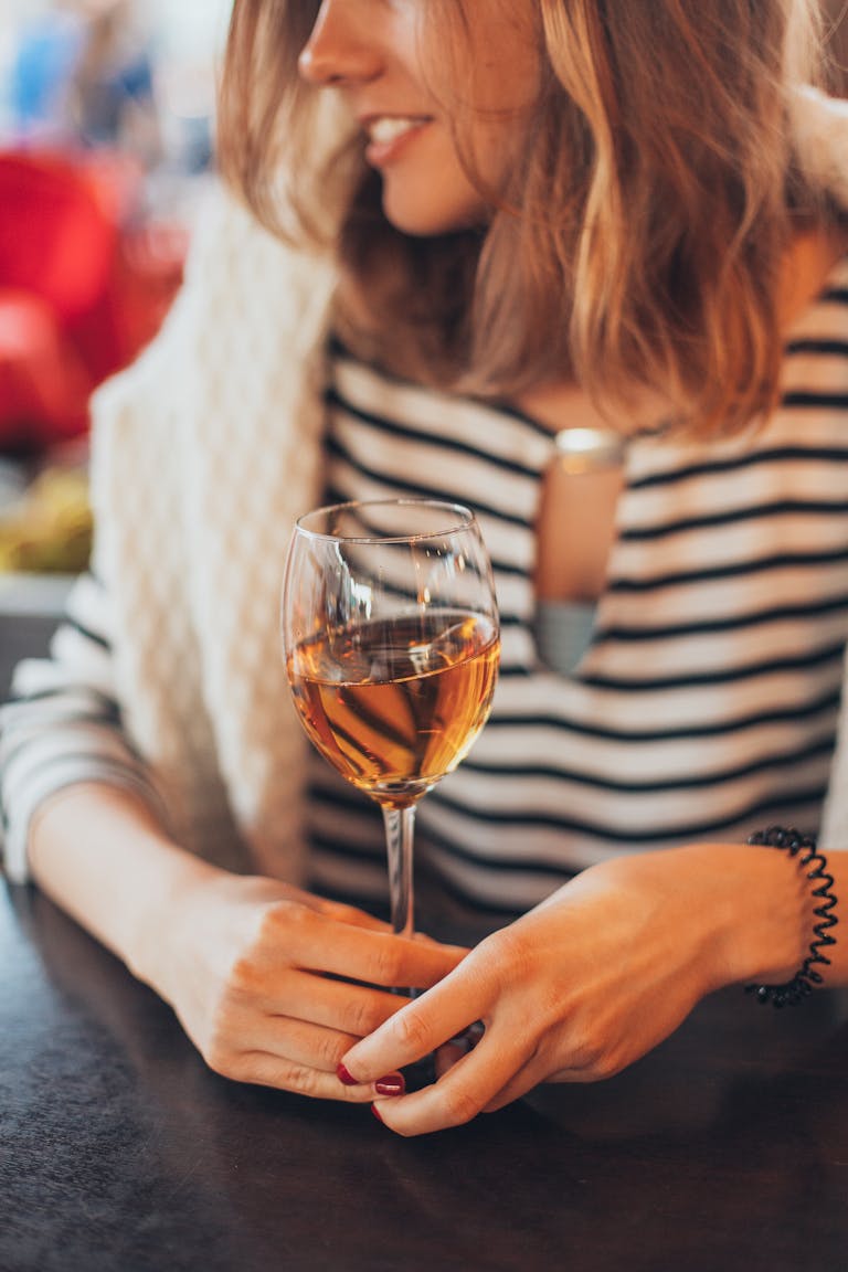 A woman with striped shirt holding a wine glass indoors, creating a warm and fashionable ambiance.