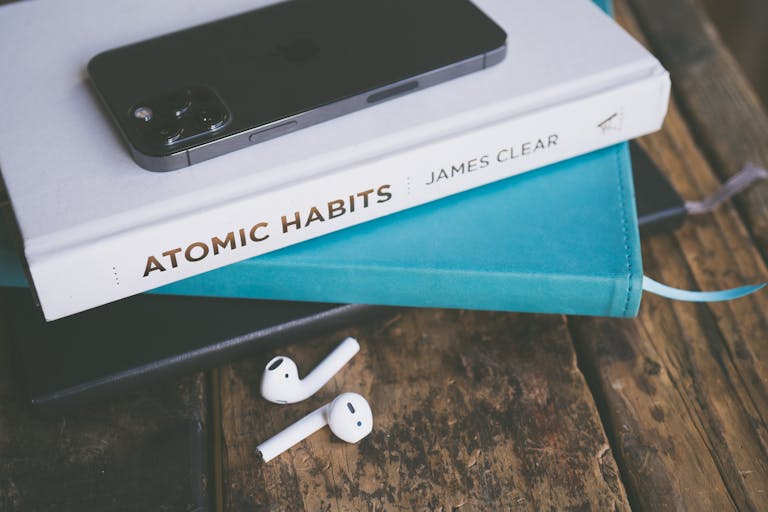 An elegant arrangement of a smartphone, book, and AirPods on a wooden table.