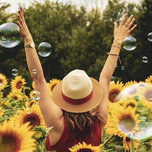 A joyful woman in a sunflower field with bubbles, expressing happiness on a summer day.